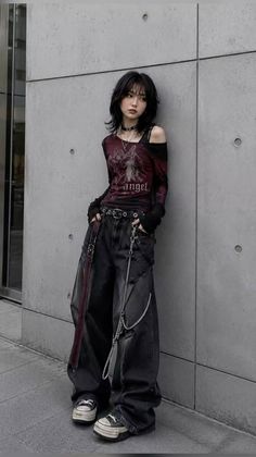 Woman in gothic-style clothing with baggy jeans and a layered top against a concrete wall