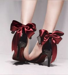 Pair of black patent leather high heels with large red bows on the ankles