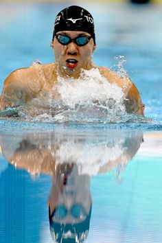 Swimmer with a black cap and goggles emerging from blue water with a splash