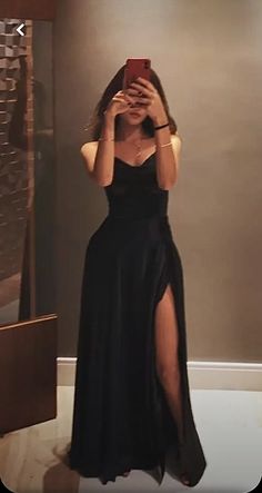 Woman in a black strapless dress with a high slit taking a mirror selfie