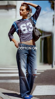 Woman in a cropped top and ripped jeans with earbuds on a sunny street
