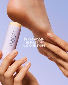 Hands applying a foot care product to a heel against a light purple background