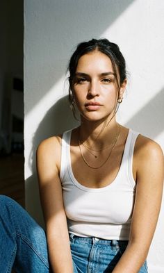 Woman in a white tank top and jeans sitting indoors with dramatic lighting