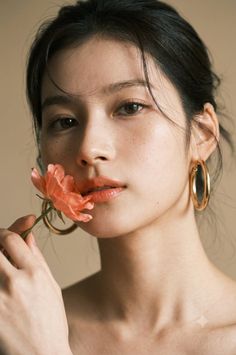 Woman with freckles and gold hoop earrings holding a pink flower to her lips