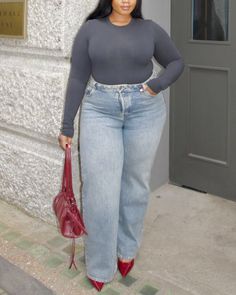 Woman in a gray long sleeve top and blue jeans holding a red handbag