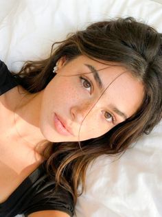 Woman with freckles and long brown hair lying on a white bed