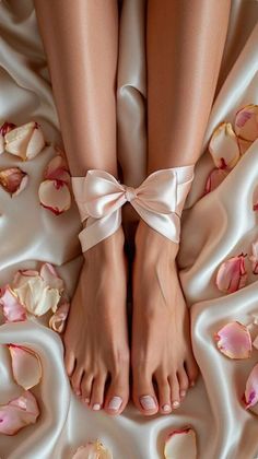 Bare legs and feet tied with a pink ribbon on silk sheets with rose petals