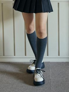 Person wearing a pleated skirt, knee-high socks, and chunky shoes indoors