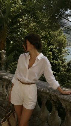 Woman in a white shirt and shorts leaning on a stone balcony outdoors