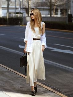 Woman with long hair and sunglasses wearing a white dress and shirt on a street