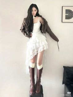 Woman with long dark hair wearing a white dress and brown jacket indoors