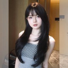 Woman with long black hair and bangs wearing a polka dot and striped top indoors
