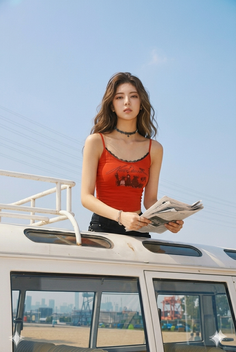 Woman with long wavy hair in a red crop top holding a newspaper on a car roof