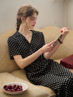 Woman in a polka dot dress reading a book on a sofa indoors