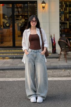 Woman in a white shirt and baggy jeans standing on a street