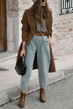 Woman in a brown coat, light wash jeans, and ankle boots on a street