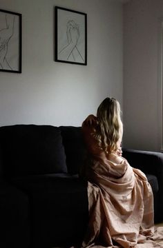 Woman with long blonde hair draped in fabric, sitting on a couch indoors