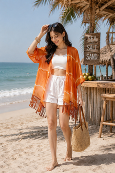 Woman in an orange kimono and white shorts walking barefoot on a beach