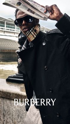 Person in a black coat and sunglasses holding a newspaper over their head in the rain
