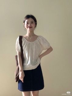 Woman in a white blouse and dark skirt with a shoulder bag indoors