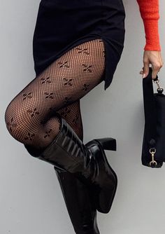 Woman in fishnet stockings, black skirt, and high boots holding a black handbag