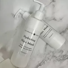 Two white bottles of hydrating hair mask with pump dispensers on a marble surface