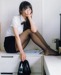 Woman in a white shirt and black skirt with pantyhose sitting indoors
