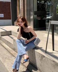 Woman with long hair in a black top and blue jeans sitting outdoors