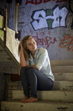 Woman with blonde hair sitting barefoot on concrete stairs with graffiti wall