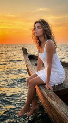 Woman in a white dress sitting on a wooden boat with her feet in the ocean at sunset