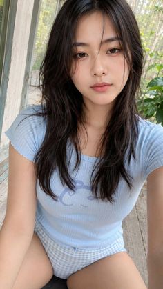 Woman with long dark hair wearing a blue top and plaid shorts outdoors
