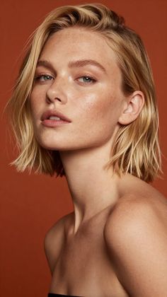 Woman with short blonde hair and freckles against a warm background