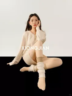 Woman in a beige sweater and leg warmers sitting on a two-tone background