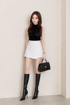 Woman in a black top, white skirt, and black boots holding a handbag