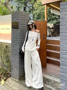 Woman in a white off-shoulder top and wide-leg pants standing outdoors