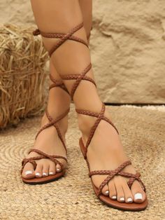 Person wearing brown braided gladiator sandals with white nail polish on a straw mat