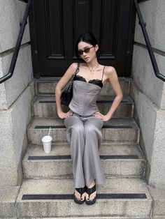 Woman in a gray corset top and wide leg pants sitting on stone steps