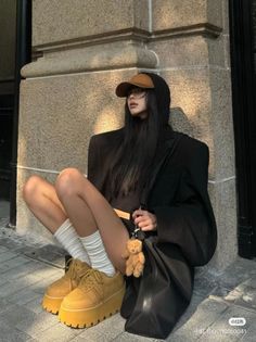 Woman with long black hair wearing an oversized blazer and platform shoes, sitting outdoors