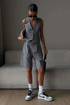 Person in a gray vest and shorts with sunglasses and sneakers indoors