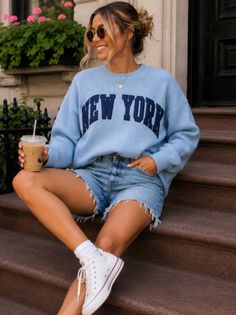 Woman in a blue 'New York' sweater and denim shorts sitting on steps
