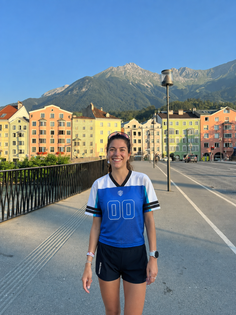 Woman in a blue jersey and shorts on a bridge with colorful buildings and mountains