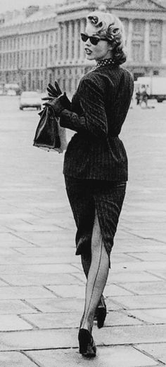 Woman in a skirt suit, sunglasses, and seamed stockings walking outdoors