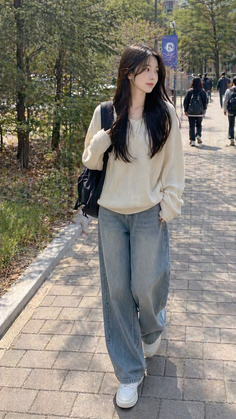 Woman with long dark hair wearing a loose sweater and baggy jeans walking outdoors