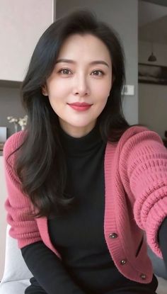 Woman with long dark hair wearing a pink cardigan and black turtleneck indoors
