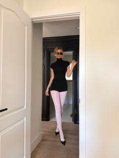 Woman in a black turtleneck and white tights posing in a doorway
