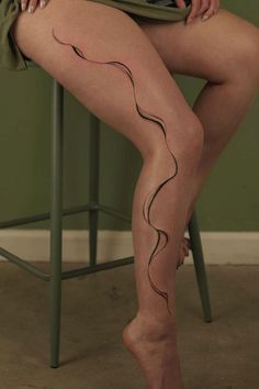 A person's legs with a minimalist abstract line tattoo on one leg