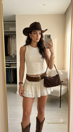Woman in a cowboy hat and boots taking a mirror selfie indoors