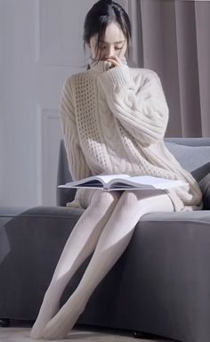 Woman in a white turtleneck sweater and tights sitting on a couch with a book
