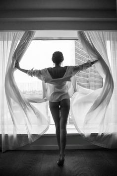 Woman in a white shirt opening curtains in a hotel room, seen from behind