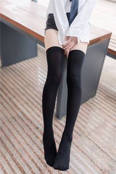 Person in a white shirt, black shorts, and thigh high socks sitting indoors